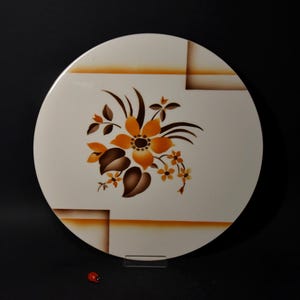 Puede incluir: Un plato redondo de cerámica blanca con un diseño floral en tonos marrones, naranjas y amarillos. El plato tiene un patrón geométrico en el fondo.