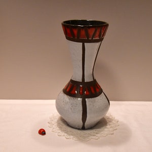 Könnte beinhalten: Eine weiße Keramikvase mit schwarzen und roten geometrischen Mustern. Die Vase hat einen schmalen Hals und einen breiten Boden.