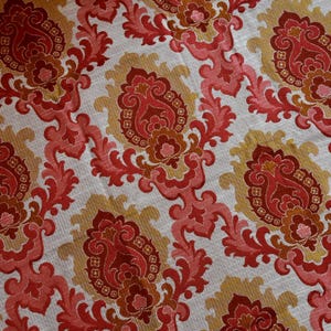Puede incluir: Tela de damasco con estampado rojo y dorado sobre fondo blanco. La tela tiene un patrón repetitivo de motivos florales estilizados.