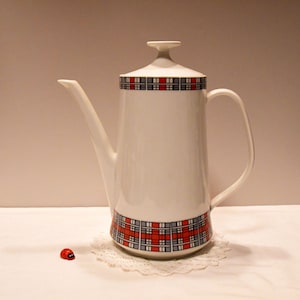 Könnte beinhalten: Weiße Kaffeekanne aus Keramik mit einem rot-schwarz-grauen Karomuster um die Basis und den Deckel. Die Kanne hat einen Ausguss und einen Griff.