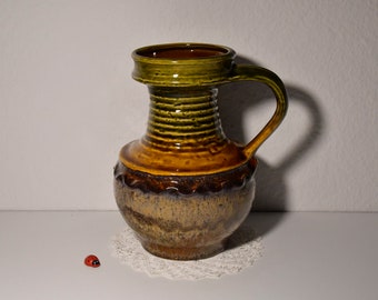 May include: A brown and green ceramic vase with a wide mouth and a handle. The vase has a textured surface and a brown glaze.