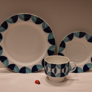 Könnte beinhalten: Ein Set aus blau-weiß gemustertem Keramikgeschirr, bestehend aus einem großen Teller, einem kleineren Teller und einer Teetasse. Das Geschirr hat ein geometrisches Design mit blauen und türkisfarbenen Kreisen.