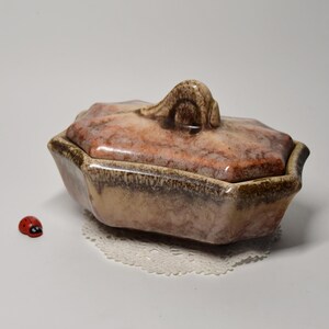 Peut inclure: Une boîte à bijoux en céramique avec un couvercle. La boîte est octogonale et a un glaçage brun, beige et rose. Le couvercle a une poignée décorative.