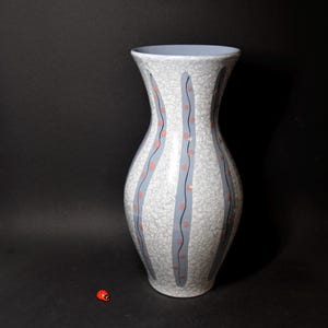 Könnte beinhalten: Eine hohe, graue Keramikvase mit craquelé-Glasur. Die Vase hat eine breite Öffnung und einen schmalen Boden. Sie ist mit vertikalen Streifen in Blau und Rosa sowie kleinen rosa Punkten verziert.