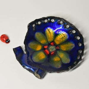 May include: A blue ceramic dish with a yellow and red flower design. The dish has a scalloped edge and is slightly chipped.