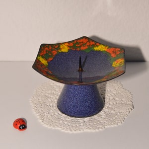 Könnte beinhalten: Ein blauer Kerzenhalter aus Keramik mit einem bunten Blumendesign. Der Halter hat einen spitzen Dorn in der Mitte für eine Kerze.