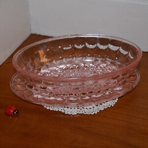 Könnte beinhalten: Eine rosa Glasschüssel mit strukturierter Oberfläche steht auf einer weißen Spitze. Die Schüssel befindet sich auf einer Holzoberfläche.