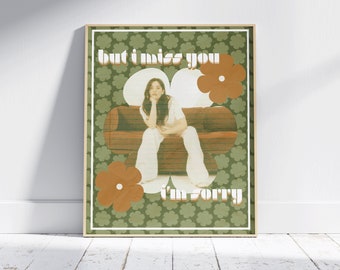 May include: A retro-style poster with a green and brown floral pattern. The poster features a woman sitting on a couch with the text "but i miss you i'm sorry" in a bold, colorful font.