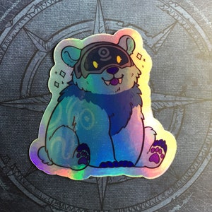Può includere: Un adesivo olografico con un orso di cartone animato blu e bianco che indossa una maschera nera con un design a spirale. L'orso è seduto con le zampe davanti a sé e ha un'espressione felice sul viso.