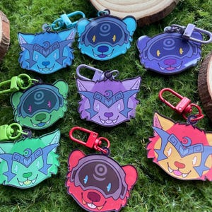 May include: A set of eight colourful keychains featuring cartoon animal faces with a crescent moon and a circle design. The keychains are made of acrylic and have a metal ring for attaching to keys.