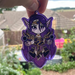 May include: Purple and black anime character keychain with a dark purple background. The character has long purple hair, a gold crown, and is holding two dark purple orbs.