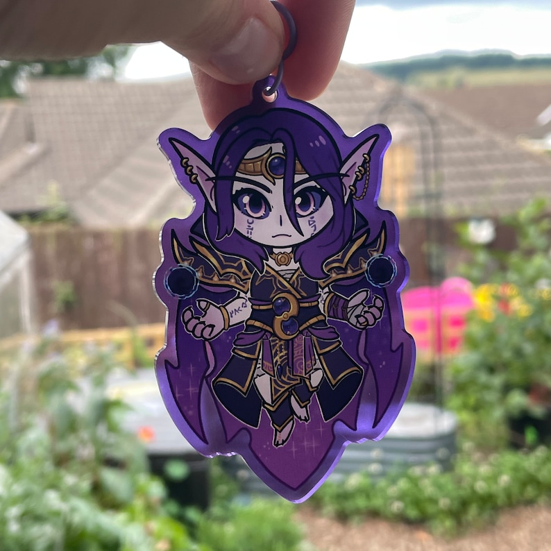May include: Purple and black anime character keychain with a dark purple background. The character has long purple hair, a gold crown, and is holding two dark purple orbs.