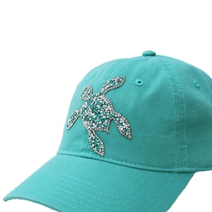Pode incluir: Um boné de beisebol azul turquesa com um design de tartaruga marinha de strass.