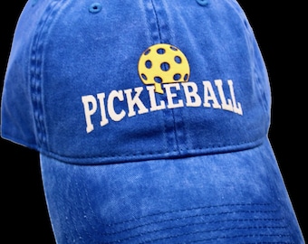 Puede incluir: Una gorra de béisbol azul con una pelota de pickleball amarilla y la palabra "PICKLEBALL" bordada en blanco.