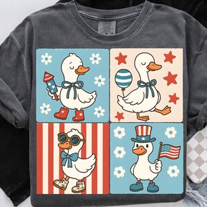 May include: A gray t-shirt with a four-panel design featuring cartoon ducks in red, white, and blue patriotic outfits. Each duck is wearing a different outfit, including a firecracker, a balloon, a top hat, and an American flag.