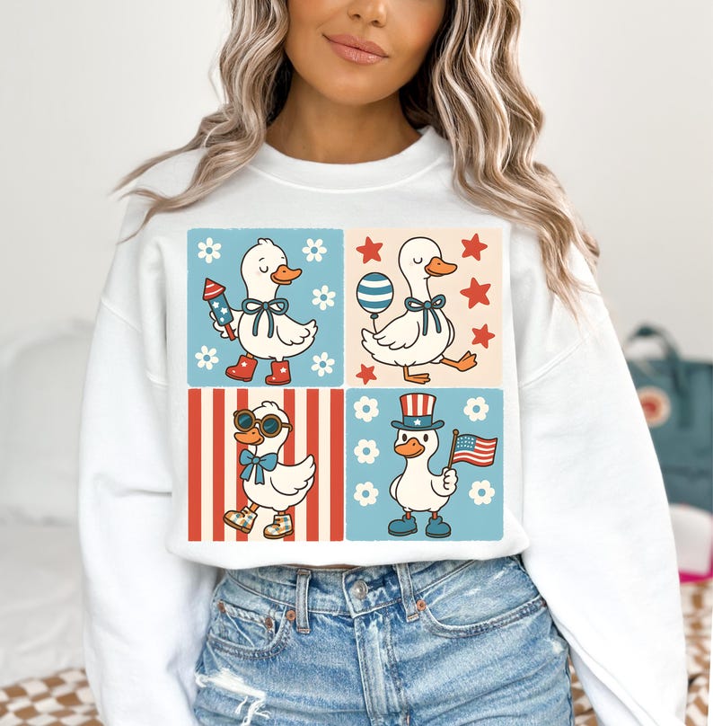 May include: White sweatshirt with a graphic of four cartoon ducks wearing patriotic accessories. The ducks are in a grid pattern with red, white, and blue stripes and stars. The text on the sweatshirt says "Duck, Duck, Goose".