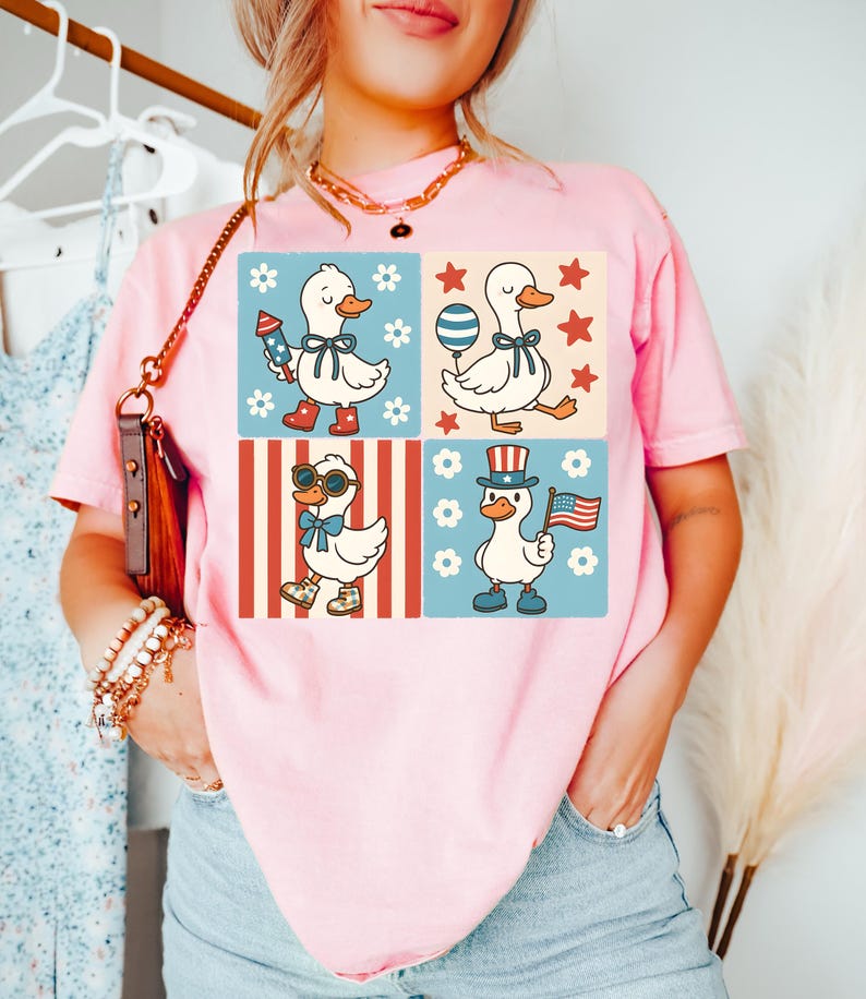 May include: Pink t-shirt with a graphic of four cartoon ducks in different patriotic outfits. The ducks are wearing sunglasses, a top hat, a bow tie, and holding a firework. The graphic is set against a red, white, and blue background.