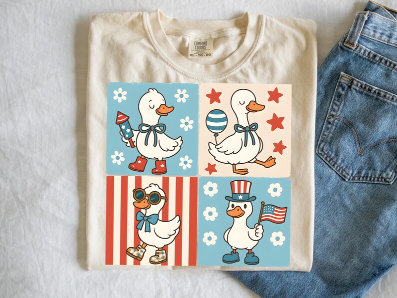 May include: A white t-shirt with a design of four cartoon ducks wearing patriotic outfits. The ducks are wearing red, white, and blue clothing and accessories. The design is on a cream background with red and white stripes and blue and white stars.