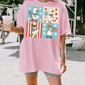 May include: A pink oversized t-shirt with a graphic print of four cartoon ducks in different patriotic themed outfits. The ducks are wearing sunglasses, a top hat, a bow tie, and a red, white, and blue bandana.