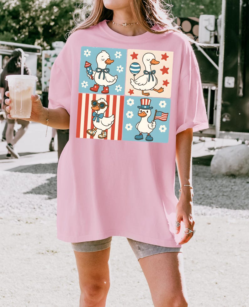 May include: A pink oversized t-shirt with a graphic print of four cartoon ducks in different patriotic themed outfits. The ducks are wearing sunglasses, a top hat, a bow tie, and a red, white, and blue bandana.