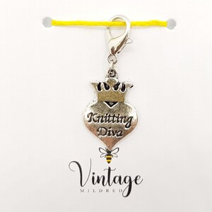 May include: Silver knitting stitch marker with a heart-shaped charm that says "Knitting Diva" and a crown on top. The charm is attached to a silver lobster clasp. The background is white with the text "Vintage Mildred" in black.