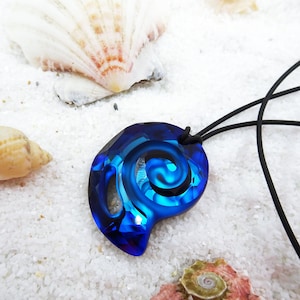 May include: A blue glass pendant with a spiral design hangs from a black cord. The pendant is on a white surface with seashells.