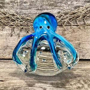 Pulpo de vidrio transparente soplado a mano con forma de remolino azul y verde que sujeta el cuerpo.