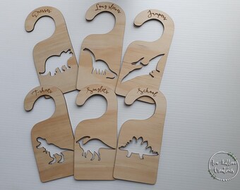 Puede incluir: Seis perchas de puerta de madera con siluetas de dinosaurios y etiquetas para diferentes prendas: Vestidos, Mangas largas, Jerseys, Camisetas, Camisetas sin mangas, Escuela.