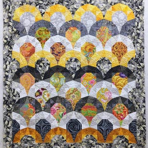 May include: A quilt with a geometric pattern of yellow, gray, and white fabric. The quilt is made up of many small pieces of fabric sewn together to create a repeating pattern.