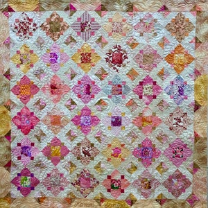 Puede incluir: Una colcha con un diseño de patchwork que presenta varios tonos de rosa, rojo y marrón. La colcha está hecha de cuadrados y diamantes, y la tela está estampada con flores, hojas y otros diseños. La colcha está firmada "Karen Sonuga" en la esquina inferior derecha.