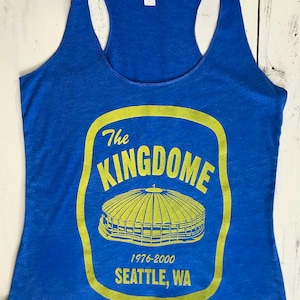 May include: A royal blue tank top featuring a yellow graphic of the Kingdome, a domed stadium in Seattle, Washington. The graphic includes the text "The Kingdome", "1976-2000", and "Seattle, WA".