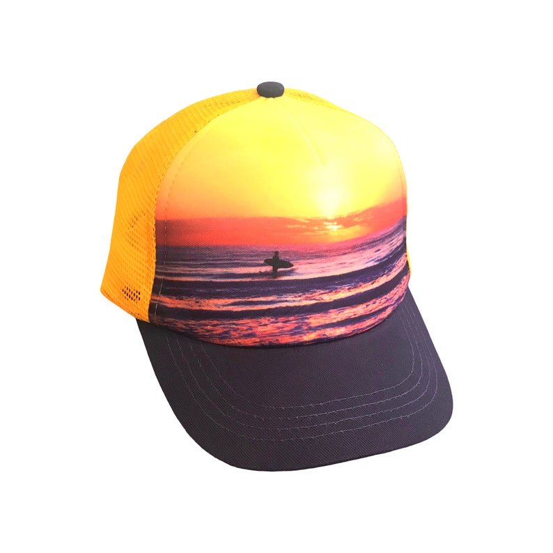 May include: A yellow and black mesh trucker hat with a sunset and surfer graphic. The hat has a black brim and a yellow mesh back.