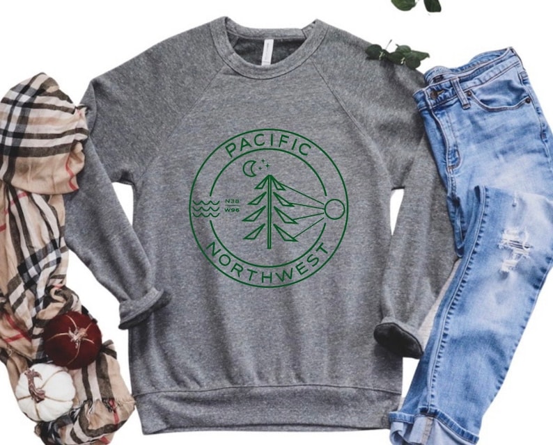 May include: Gray sweatshirt with a green circle graphic that says "Pacific Northwest" with a stylized evergreen tree, moon, sun, and waves inside the circle.