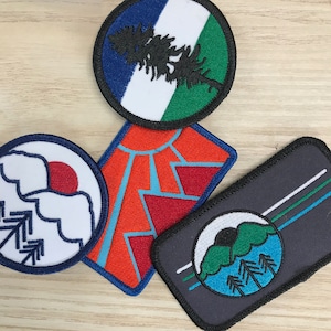 Può includere: Quattro toppe ricamate da stirare con diversi design. Una toppa presenta un design blu, bianco e verde con un pino. Un'altra toppa presenta un design rosso, bianco e blu con una catena montuosa. Una terza toppa presenta un design bianco e blu con una montagna e alberi. L'ultima toppa presenta un design nero, bianco e verde con una montagna e alberi.