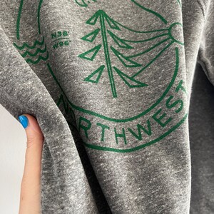 May include: Gray sweatshirt with a green circular graphic design featuring a stylized pine tree, a crescent moon, and the text "PACIFIC NORTHWEST".