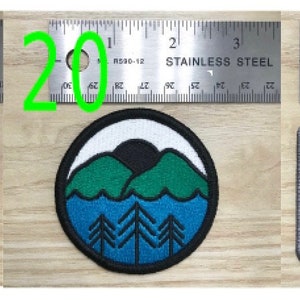 May include: Three embroidered patches featuring black, white, blue and green thread. The first patch is black with white stripes and the text "HILLTOP Tacoma". The second patch is blue with a white background and a green mountain scene. The third patch is black with a yellow crescent moon and the text "EAST SIDE Tacoma" in blue.