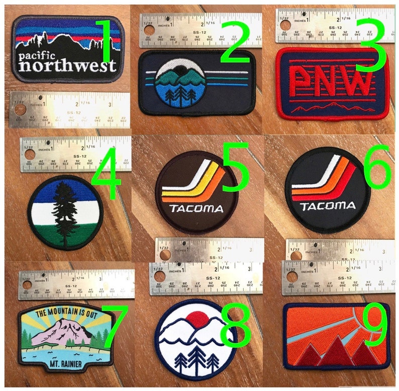 May include: Nine embroidered patches with various designs, including a mountain range, a pine tree, and the words "Pacific Northwest" and "Tacoma".