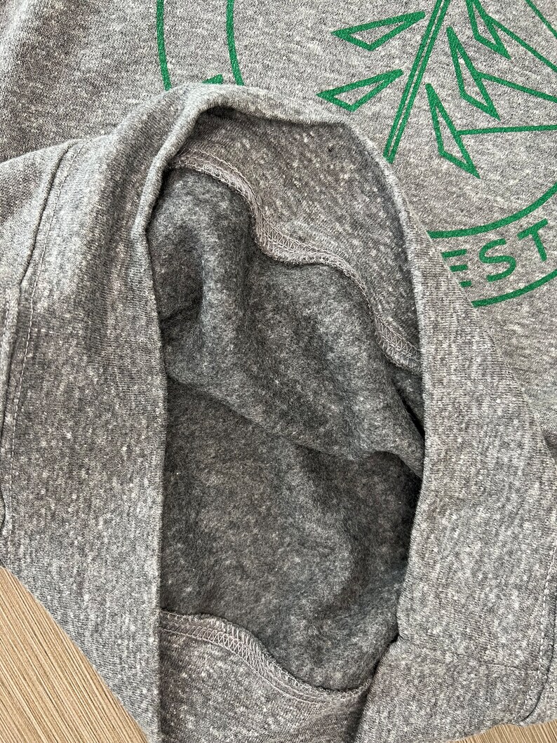May include: A close-up of the inside of a gray heather t-shirt with a green graphic of a stylized pine tree and the text "EST."