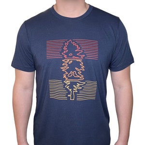 May include: A navy blue t-shirt with a graphic of a stylized tree in orange, yellow, and red lines. The tree is repeated three times, with each repetition having a different color scheme.