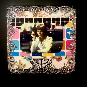 May include: A framed image featuring a woman in a white shirt, holding a cigarette. The frame is decorated with rhinestones and colorful patterned paper. The text "ARE YOU EXPERIENCE" is visible.