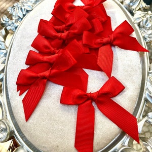 May include: A set of ten red satin ribbon bows, arranged in a decorative pattern on a white background. The bows are tied with a simple knot and have a classic, elegant look.