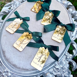 May include: Five gold mirror acrylic tags with green satin ribbon bows. Each tag has the text "Tiandra & Tyray" and a letter T in a decorative font.