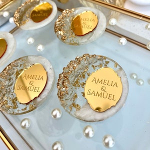 May include: Four round, white, resin coasters with gold flakes and a gold mirror-like disc in the center. Each disc has the text "Amelia & Samuel" engraved on it.