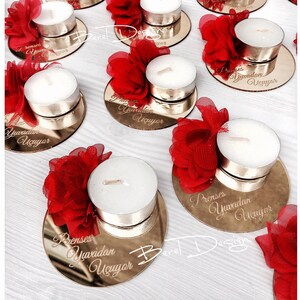 May include: Gold mirrored round candle holders with red fabric flowers and white tea light candles. Each holder has the text "Prenses Yuvadan U&ccedil;uyor" engraved on the surface.