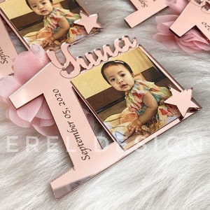 Puede incluir: Tres decoraciones de primer cumplea&ntilde;os de acr&iacute;lico rosa con un marco de fotos y un adorno de flor rosa. Cada decoraci&oacute;n tiene el nombre "Yuna" y la fecha "Septiembre 05, 2020" impresa en ella.