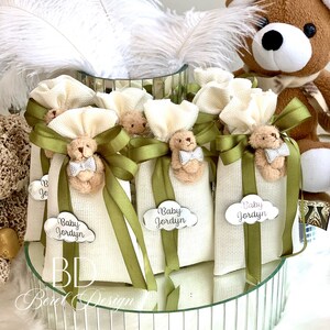 May include: White fabric bags with green ribbon and a small teddy bear charm. Each bag has a silver tag with the text "Baby Jordyn".