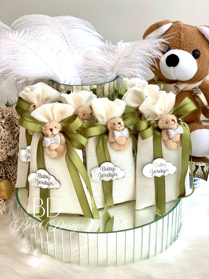 May include: White fabric bags with green ribbon and a small teddy bear charm. Each bag has a silver tag with the text "Baby Jordyn".