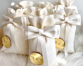 May include: Five white fabric gift bags with white satin ribbon bows and gold round tags with the initials "A & S" printed on them.