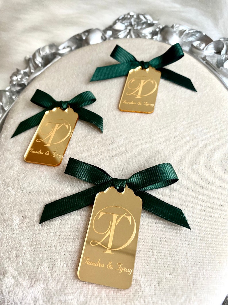 May include: Three gold mirror acrylic tags with green ribbon bows. Each tag has a cursive letter 'T' and 'D' intertwined and the text "Tiandra & Tyray" below.