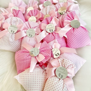 May include: Pink and white fabric gift bags with a silver circle tag that says "Baby Bassalali" in a cursive font. The bags are tied with a pink ribbon.
